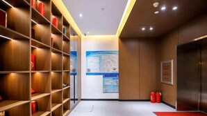 A hallway with wooden shelving units, a blue informational poster, and a red carpet leading to an elevator. - Jinjiang Inn (Changchun Railway Station) (Changchun)