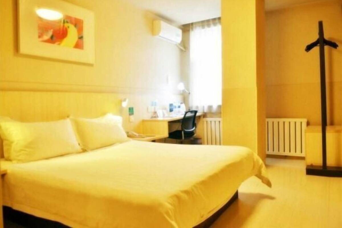 A hotel room with a bed, a desk, a chair, and a radiator.
