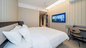 Une chambre d’hôtel comprenant un lit, un bureau avec une chaise, un téléviseur fixé au mur et un espace douche.