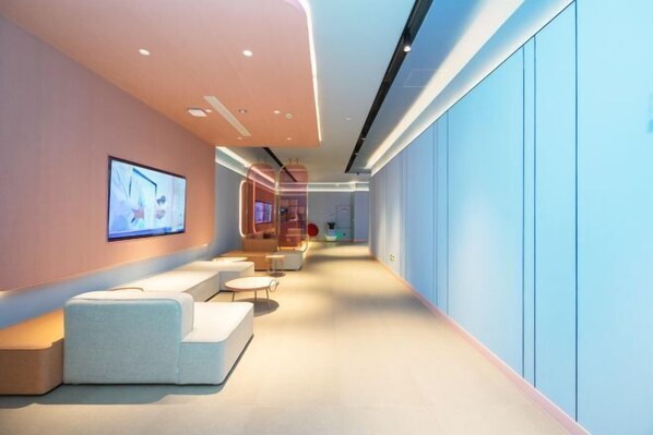 A modern interior with a long corridor, seating areas, and a television screen on the wall.