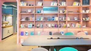 Un intérieur moderne avec une grande bibliothèque remplie de livres et d’objets décoratifs, un comptoir orné d’un logo et un espace détente avec des fauteuils.