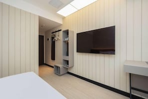 Une chambre d’hôtel moderne dotée d’un téléviseur à écran plat fixé au mur, d’un lit blanc et d’un petit coin salon avec une table et des chaises.