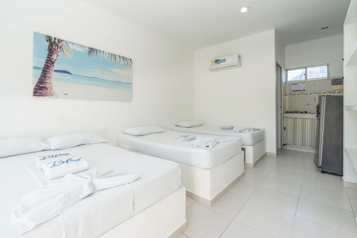 Habitación de hotel con dos camas, un cuadro de playa, una kitchenette y un refrigerador.