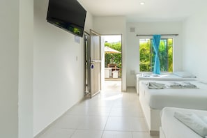 A hotel room with a TV, two beds, a window with curtains, and a view of the outdoors.