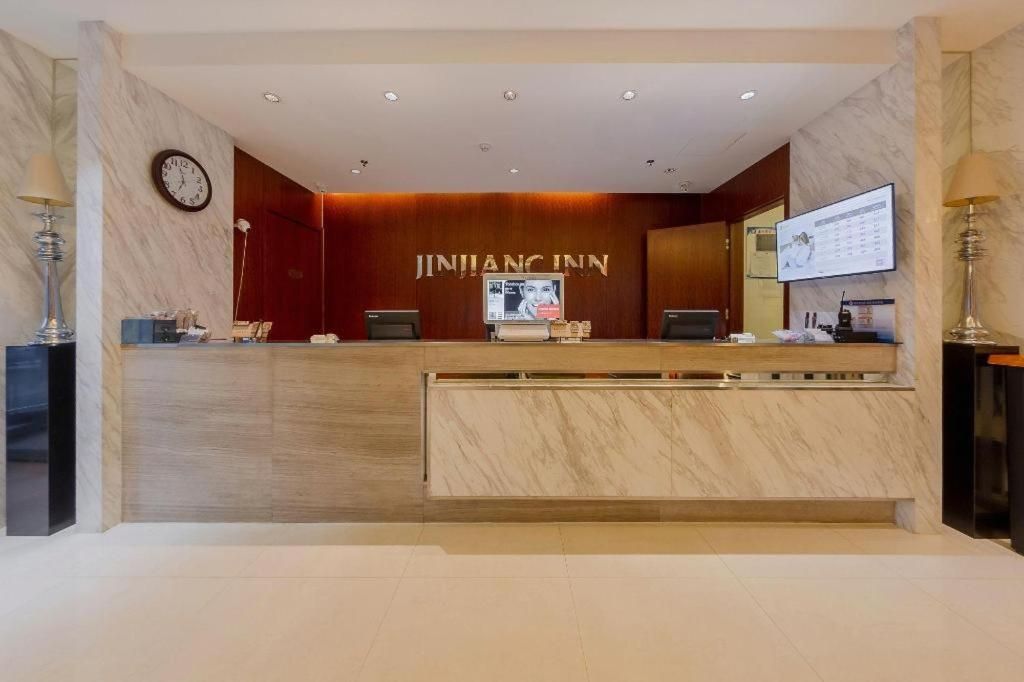 En receptionsdisk med en klocka, en tv-skärm och en väggpanel i trä med hotellets namn.