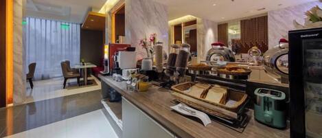 A modern hotel lobby with a marble reception desk, a seating area, and a buffet with various food items.