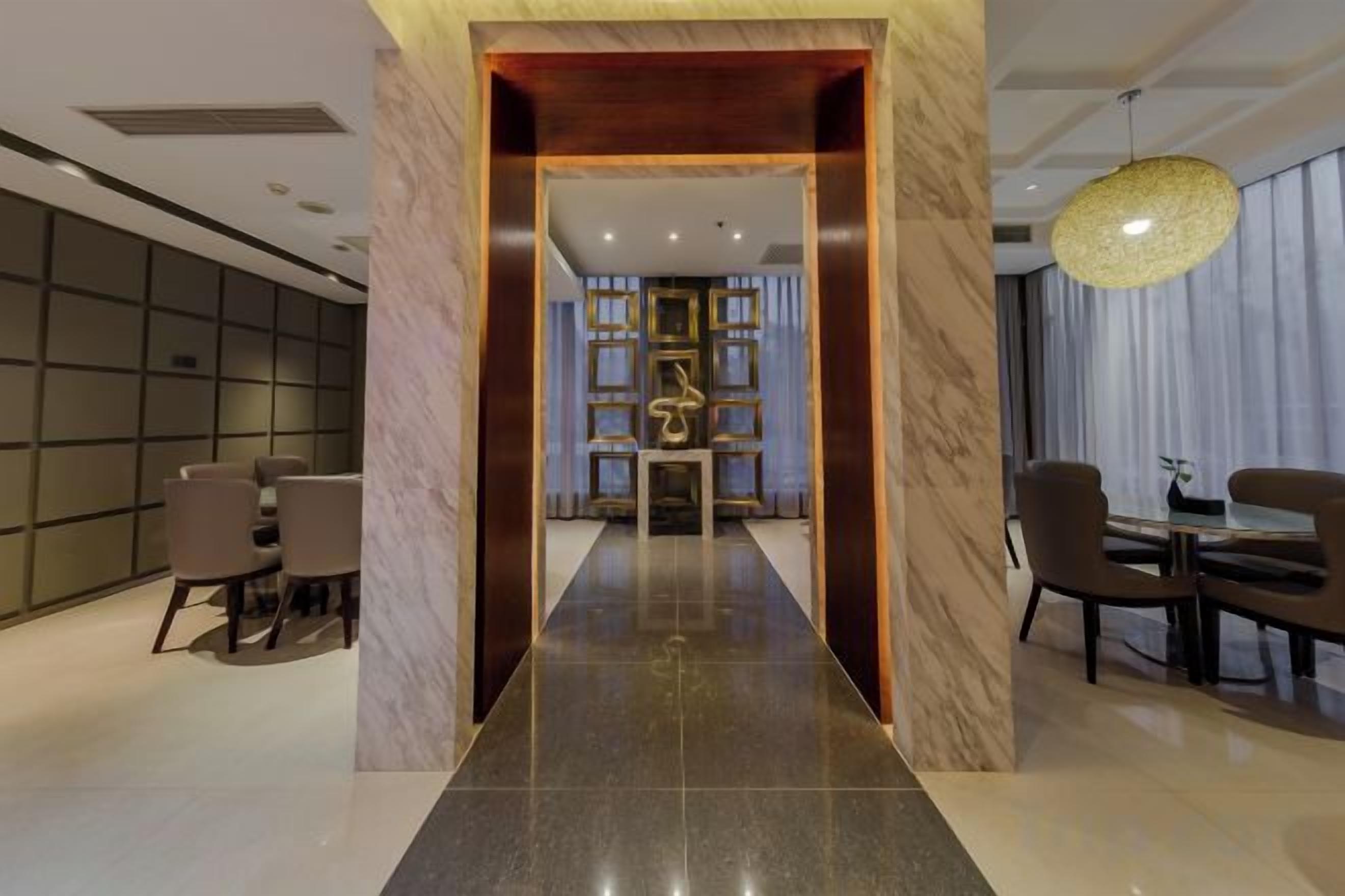 A hotel lobby with a modern design, featuring a central reception desk, a seating area with chairs, and a decorative wall with a patterned design.
