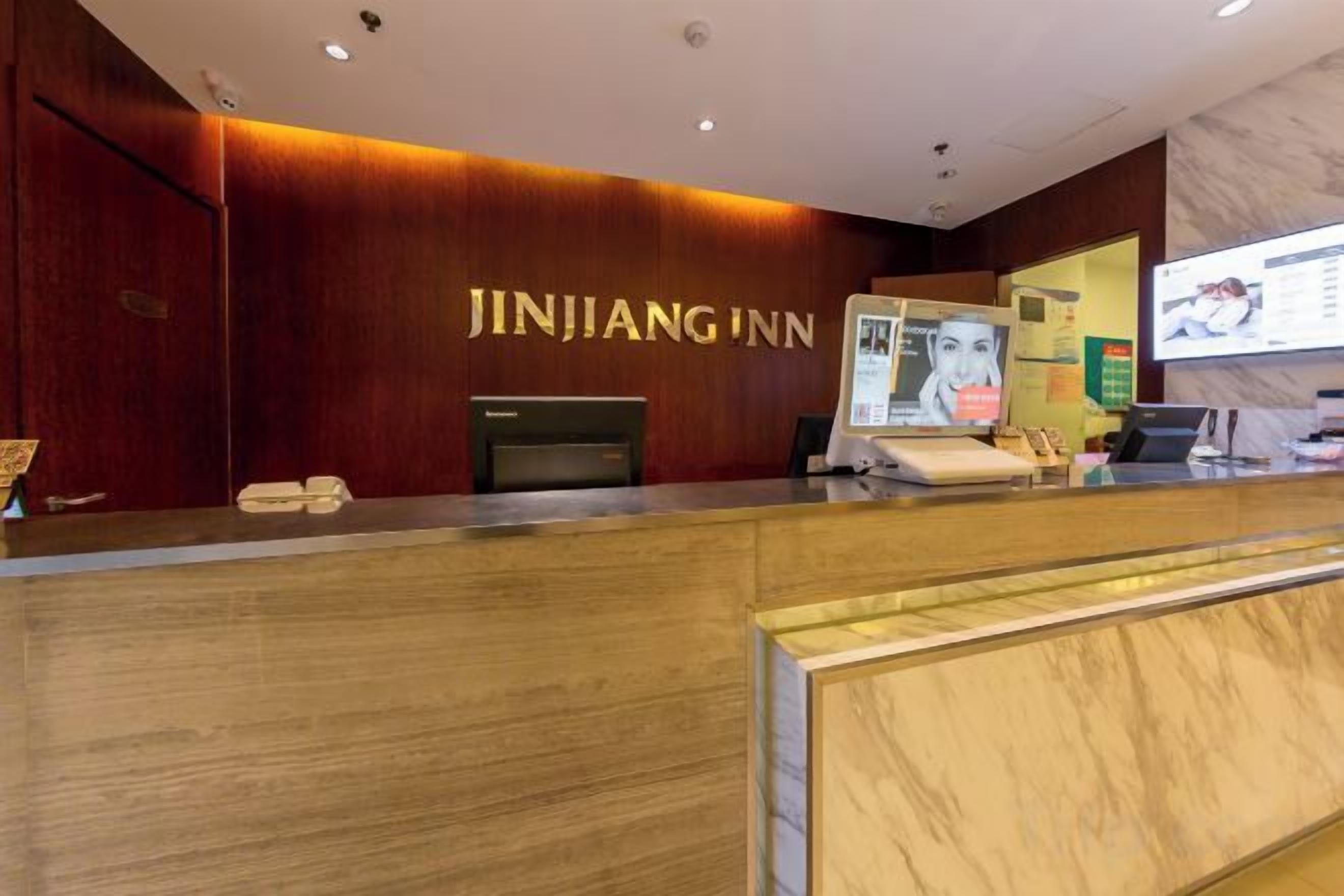 A reception desk with a wooden finish, a digital screen, and a sign reading 'JINJIANG INN'.