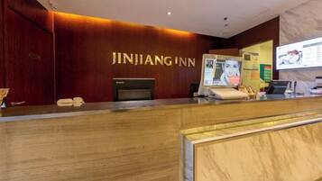 A reception desk with a wooden finish, a digital screen, and a sign reading 'JINJIANG INN'.