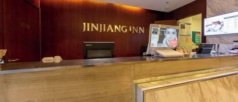 A reception desk with a wooden finish, a digital screen, and a sign reading 'JINJIANG INN'.