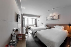 Een hotelkamer met twee bedden, een bureau met stoel, een koffiezetapparaat en een prullenbak.