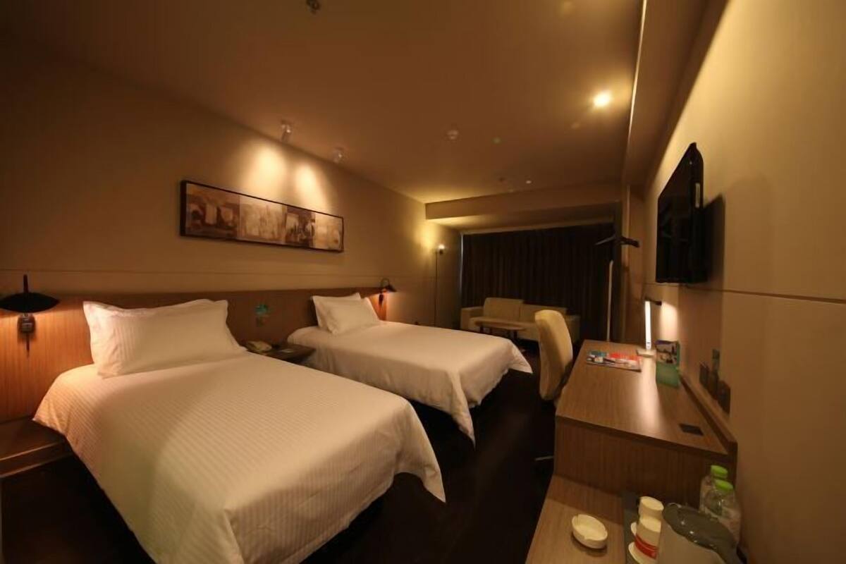 A hotel room with two beds, a desk, a chair, a TV, and a painting on the wall.