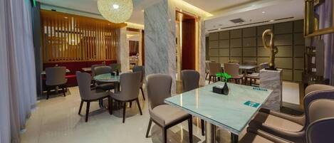 Comedor moderno de hotel con una mesa de vidrio, sillas de cuero y una lámpara colgante decorativa.