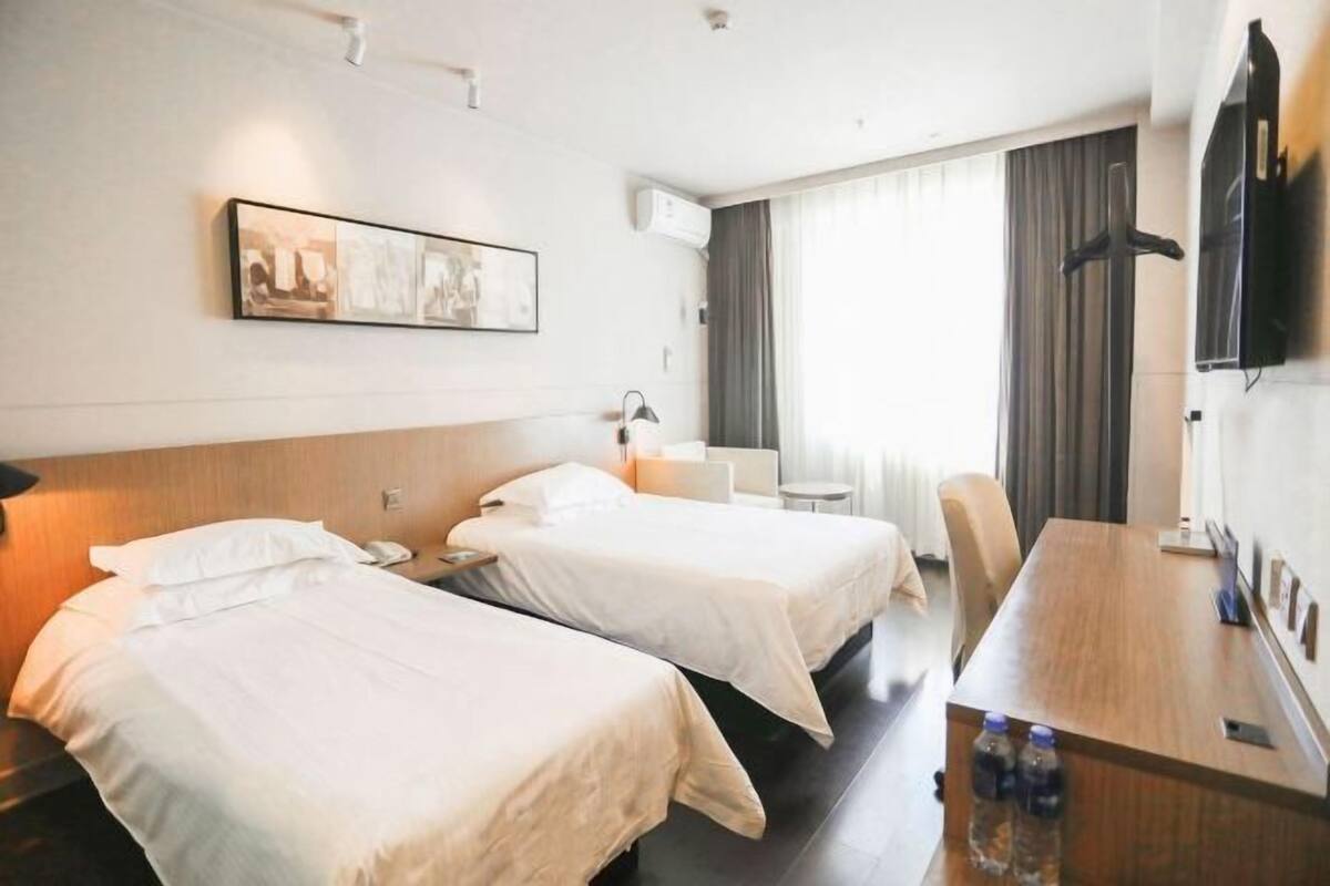 A hotel room with two beds, a desk, a chair, a TV, and a painting on the wall.