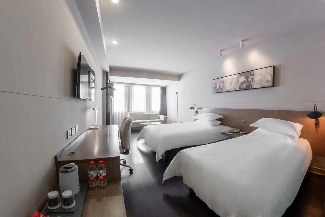 Ein Hotelzimmer mit zwei Betten, einem Schreibtisch, einem Stuhl, einem Fernseher und einem Fenster mit Vorhängen.