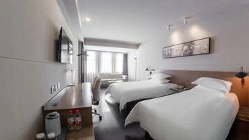 Ein Hotelzimmer mit zwei Betten, einem Schreibtisch, einem Stuhl, einem Fernseher und einem Fenster mit Vorhängen.