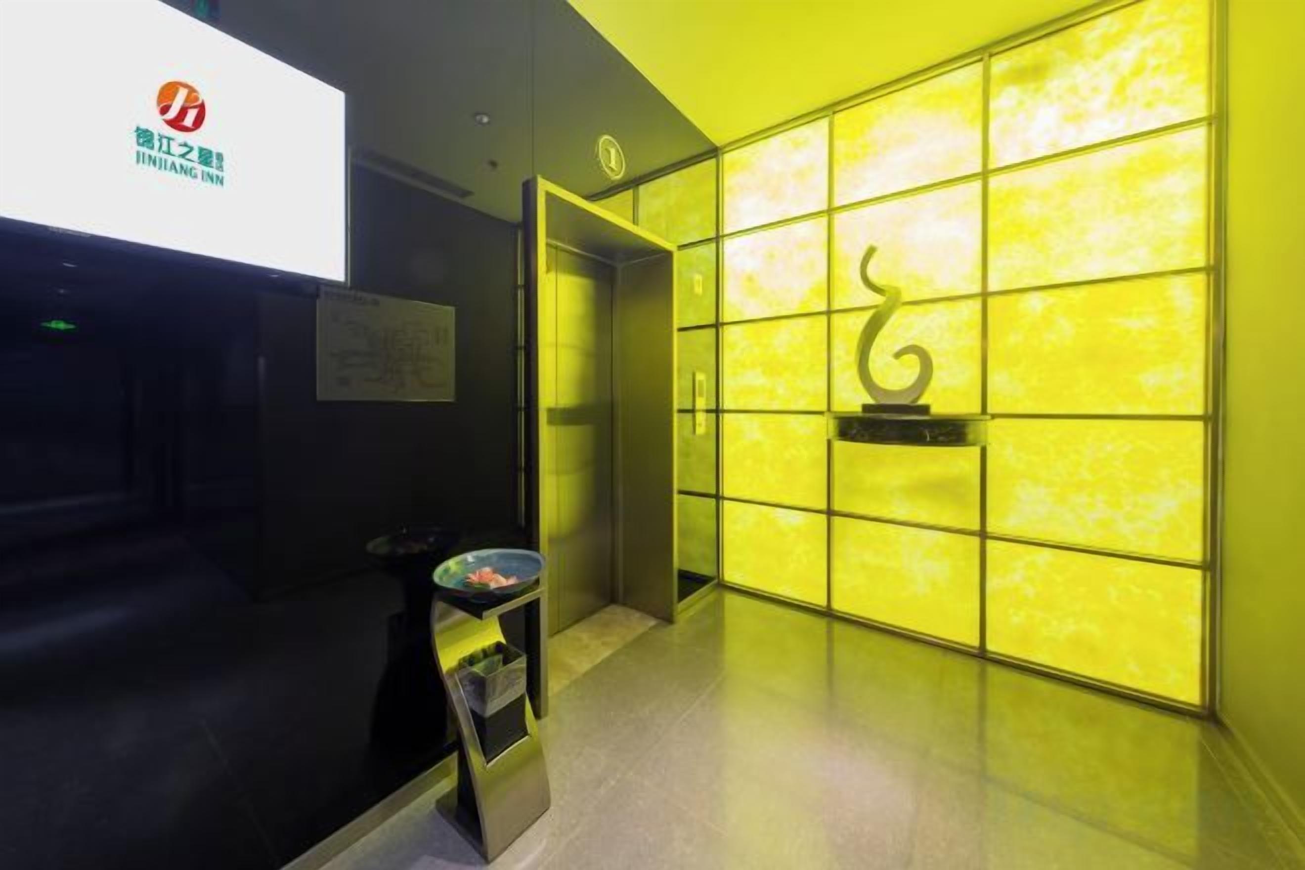 A hotel reception area with a modern design, featuring a reception desk, a digital screen, and a wall with a geometric pattern.