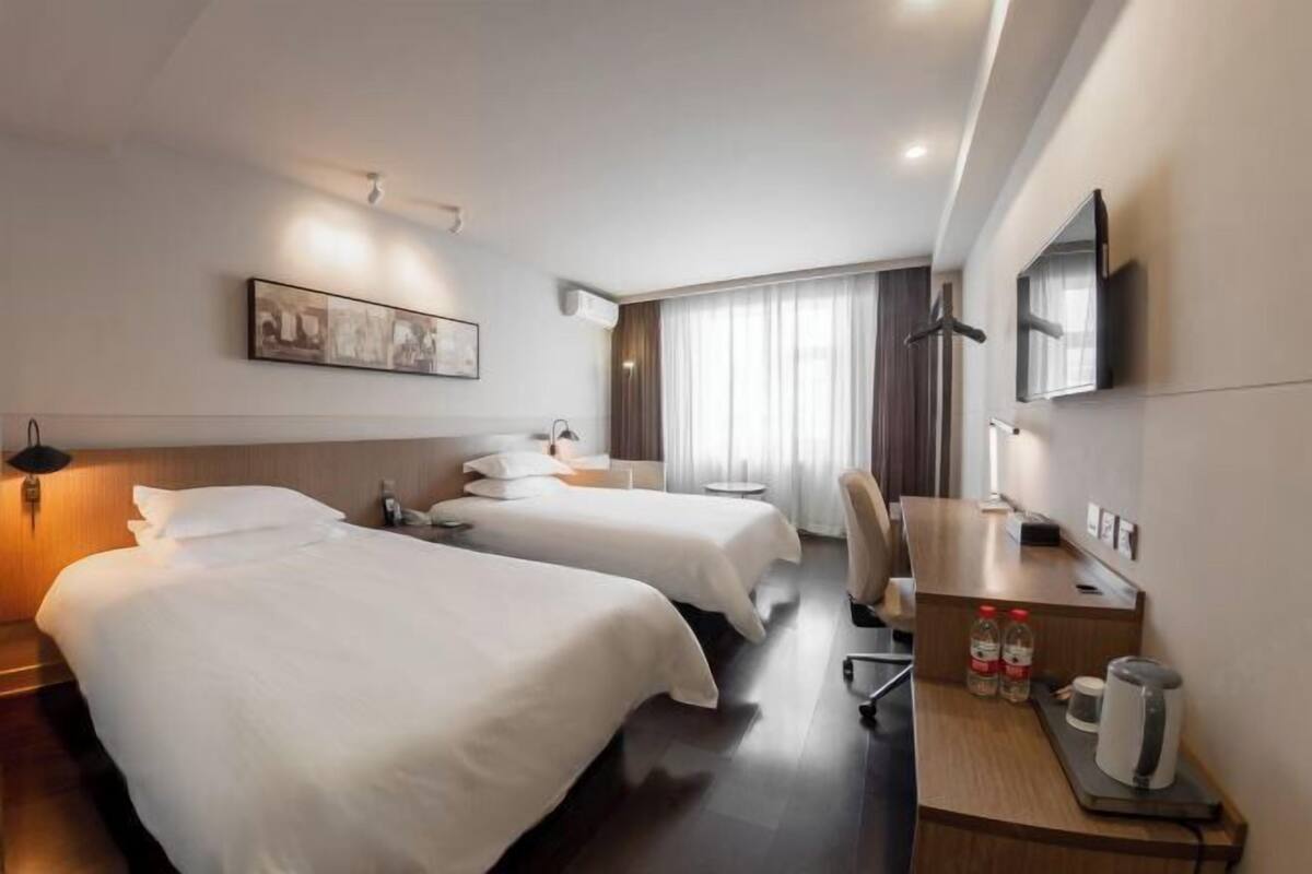 A hotel room with two beds, a desk with a chair, a television, and a painting on the wall.