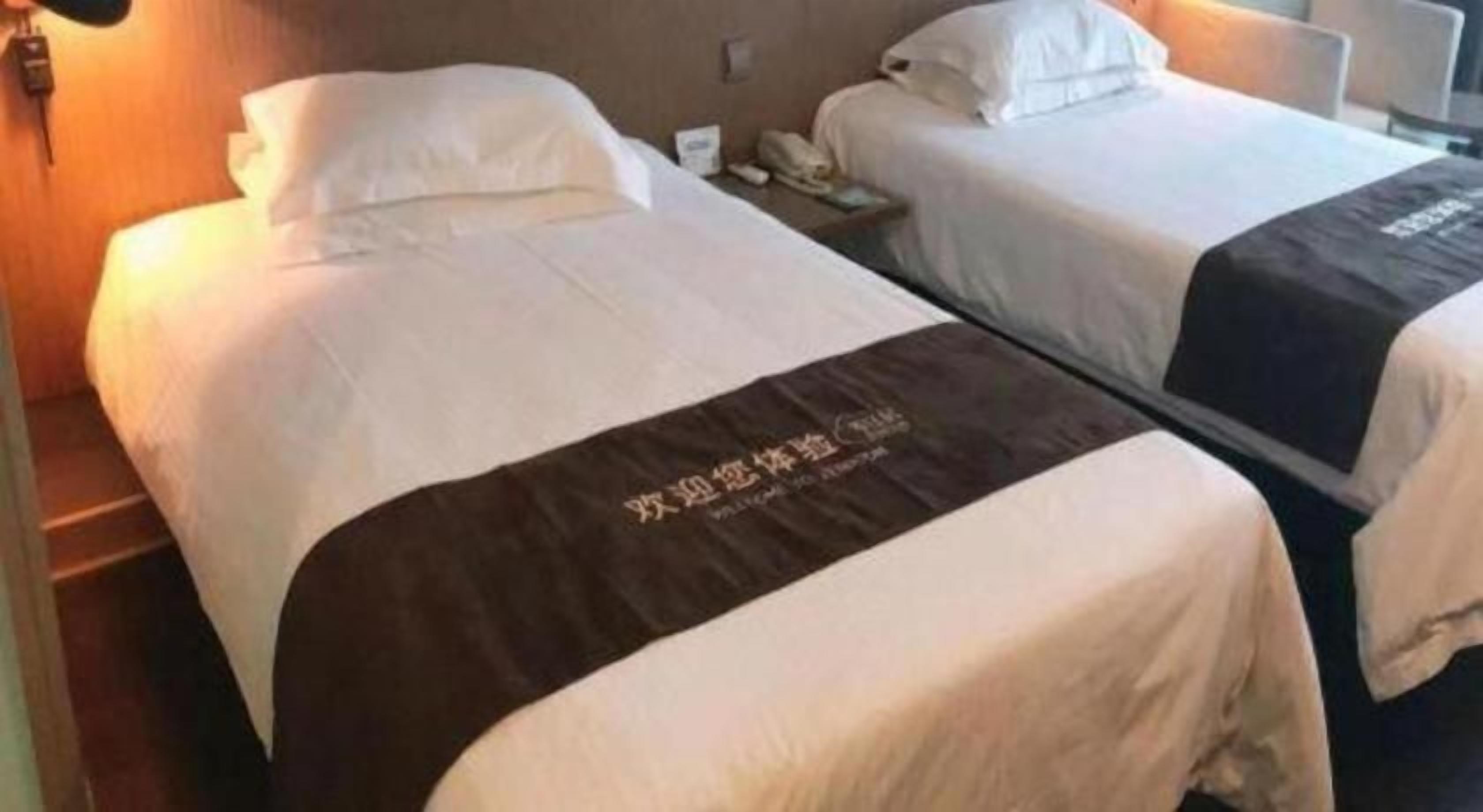 A hotel room with two beds, each with white linens and a brown headboard.