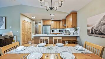 A modern kitchen with wooden cabinets, a central island, and a dining area set for four with a table, chairs, and dinnerware.