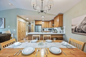 Una cocina moderna con armarios de madera, una isla central y un comedor preparado para cuatro personas, con mesa, sillas y vajilla.