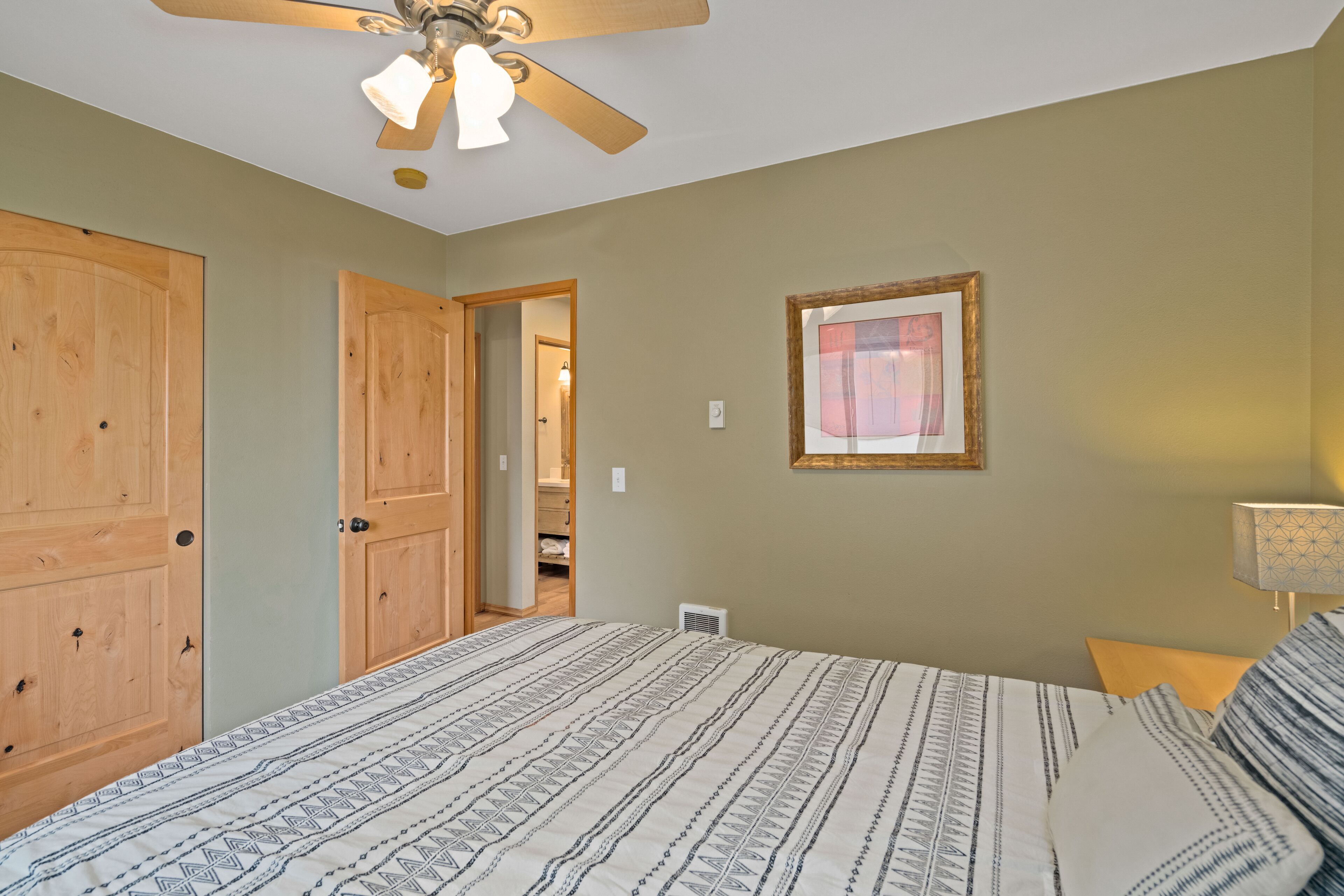 A bedroom with a bed, a ceiling fan, a door, and a framed picture on the wall.