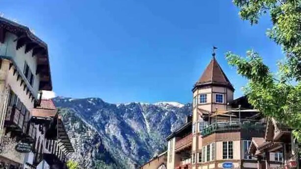 Rua em uma cidade de montanha, com edifícios tradicionais e uma montanha imponente ao fundo.