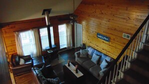 A cozy cabin interior with a wooden interior, a sofa, a coffee table, and a staircase.