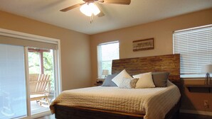 A bedroom with a bed, a ceiling fan, a window with blinds, and a chair by the window.