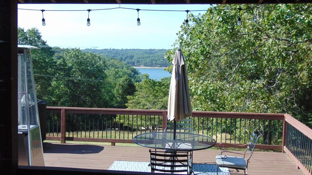 A deck with a table and chairs, overlooking a lake and forest.