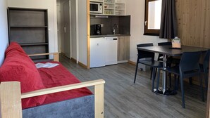 A compact living space with a kitchenette, a dining area, and a red sofa. - travelski home classic - Résidence La Muzelle. (Les Deux Alpes)