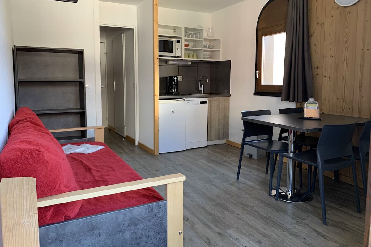 Ein gemütlicher Wohnraum mit Küchenzeile, Essbereich und einem roten Sofa.
