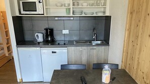 A compact kitchen with a microwave, coffee maker, and sink. There is a dining table with chairs and a remote control on it. - travelski home classic - Résidence La Muzelle. (Les Deux Alpes)