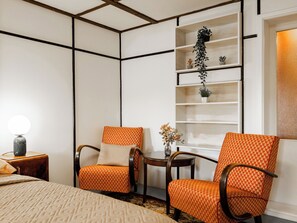 Ein Hotelzimmer mit einem Bett, zwei Sesseln, einem kleinen Tisch, einem Bücherregal und einem Fenster mit Blick.