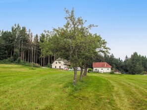Un paysage rural avec un grand champ, une maison blanche avec un toit rouge et un bâtiment plus petit en arrière-plan.
