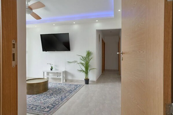 A modern living room with a flat-screen TV, a wooden floor, a round coffee table, a patterned rug, and a potted plant. - Amazing stay in zona colonial (Santo Domingo Este)