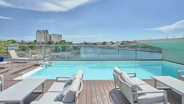 Une piscine sur le toit, avec une eau d’un bleu cristallin, entourée de chaises longues blanches et bordée d’une rambarde en verre.