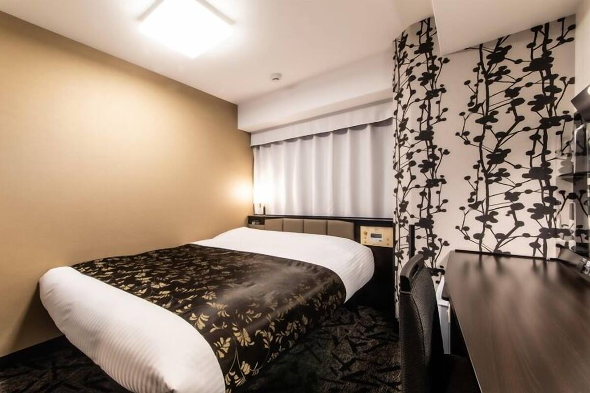 Une chambre d’hôtel comprenant un lit, une table de chevet, un bureau, un téléviseur fixé au mur et une fenêtre avec des rideaux.