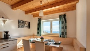 Ein gemütlicher Essbereich mit einem Holztisch, weißen Stühlen und einer Bank. Auf der Arbeitsfläche steht eine Kaffeemaschine und ein Gemälde ist an der Wand aufgehängt.