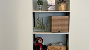 A multi-tiered shelving unit with wicker baskets, a teddy bear, and decorative items.