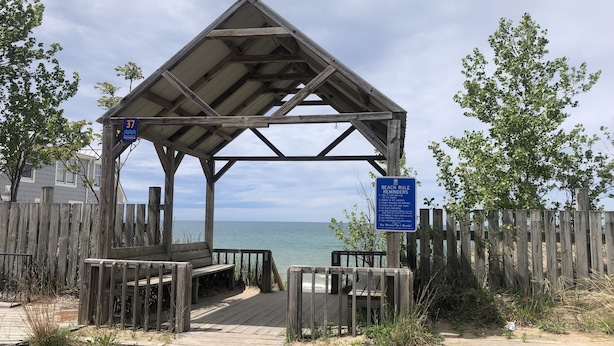 A wooden gazebo with a beach view, a wooden fence, and a sign with beach rules.