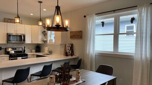 A modern kitchen with white cabinets, a stainless steel microwave, and a wooden dining table with chairs.