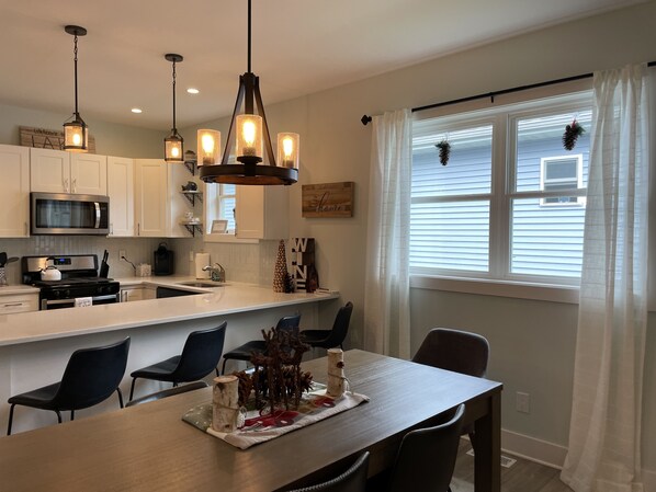 A modern kitchen with white cabinets, a stainless steel microwave, and a wooden dining table with chairs.