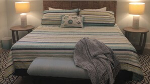 A bedroom with a large bed, two bedside lamps, a ceiling fan, and a painting above the bed.