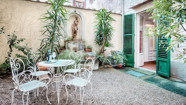 A courtyard with a statue, a table with chairs, and a building entrance. - Corte al Duomo in Florence, a cozy apartment with garden by Mmega (Firenze)
