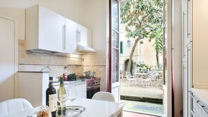 A kitchen with white cabinets, a dining table with a tray of food and wine, and a view of an outdoor patio with chairs and a tree. - Corte al Duomo in Florence, a cozy apartment with garden by Mmega (Firenze)