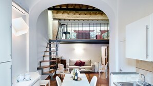 A compact kitchen with white cabinetry, a dining area with a white table and chairs, a staircase leading to a loft, and a view of the outside. - Corte al Duomo in Florence, a cozy apartment with garden by Mmega (Firenze)