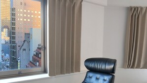 A modern hotel room with a leather armchair and ottoman, a wooden coffee table, and a large window offering a city view. - Santiago Hotel (Hiroshima)