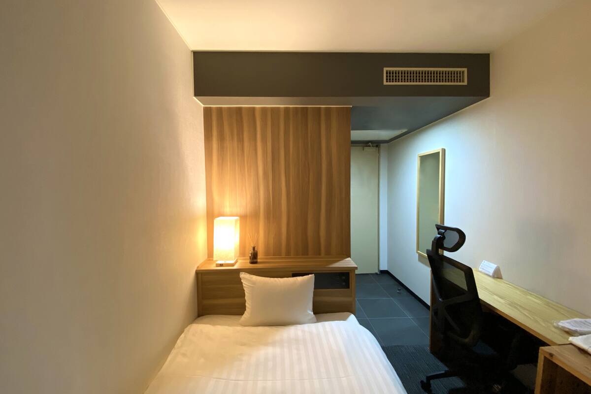 A hotel room with a bed, a desk, a chair, a lamp, and a mirror.