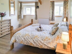 A bedroom with a wooden bed frame, floral bedding, a bedside table with a lamp, a dresser, and a window with curtains. - 2 bedroom accommodation in Carmel, near Caernarfon (Carmel, near Caernarfon)